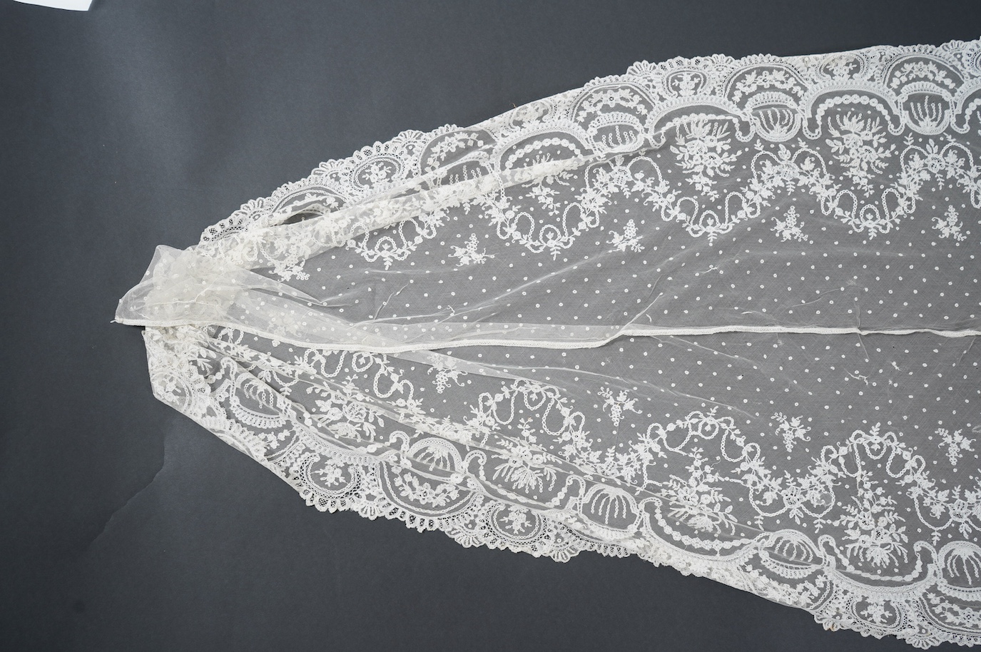 A wide flounce of fine ornate hand made 19th century Brussels bobbin lace, appliquéd onto a net ground, possibly commissioned for a wedding gown, now sewn together along the top edge and the two cut ends also stitched to
